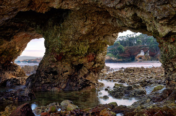 Large holes in the rock on stony coast near the Spanish Atlantic port city of Burela in Galicia. The mountain has two large stone arches. In the background the coastal landscape.