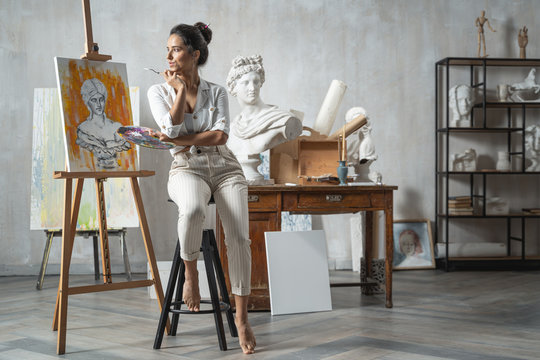 Satisfied artist posing near new picture next to easel