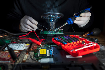 Hands of a man in white gloves repair laptop using soldering iron