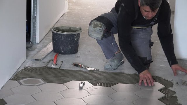 Skilled tiler lay hexagon floor tiles in corridor