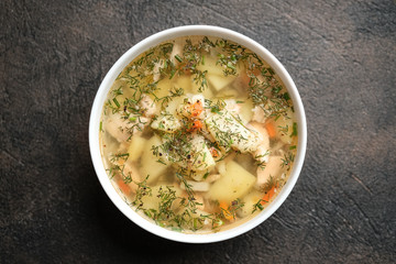 Fresh homemade fish soup with vegetables in bowl on black background, top view