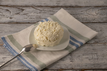 cottage cheese on a white pleta ith a spoon on a linen napkin on an old background