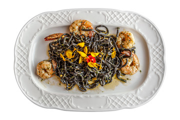 black spaghetti with king prawns in pesto decorated with yellow petals on a porcelain plate isolated on white