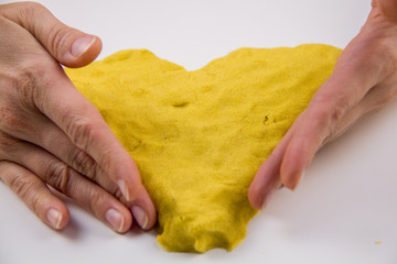 female hands mold yellow kinetic sand in the form of a heart on a white table. Antistress