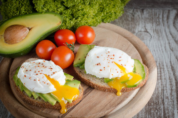 Avocado toast, cherry tomato and poached eggs on wooden background. Breakfast with vegetarian food, healthy diet concept.