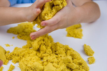 children's hands play yellow kinetic sand on a white table. Antistress