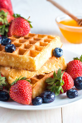 Fresh homemade food of berry Belgian waffles with honey, chocolate, strawberry, blueberry, maple syrup and cream. Healthy dessert breakfast concept with juice