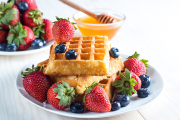 Fresh homemade food of berry Belgian waffles with honey, chocolate, strawberry, blueberry, maple syrup and cream. Healthy dessert breakfast concept with juice