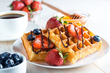 Fresh homemade food of berry Belgian waffles with honey, chocolate, strawberry, blueberry, maple syrup and cream. Healthy dessert breakfast concept with juice