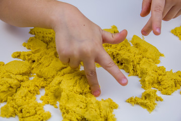 children's hands play yellow kinetic sand on a white table. Antistress
