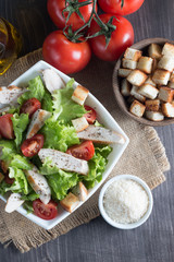 Fresh Caesar salad with delicious chicken breast, ruccola, spinach, cabbage, arugula, egg, parmesan and cherry tomato on wooden background. Oil, salt and pepper. Healthy and diet food concept.