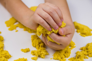 children's hands play yellow kinetic sand on a white table. Antistress