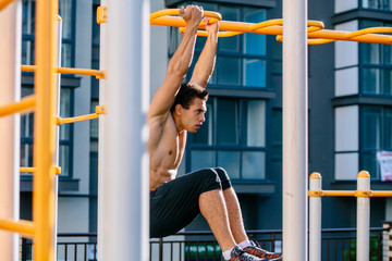 Fototapeta na wymiar Sporty man enjoying music during workout outdoors, doing chin-ups on horizontal bars