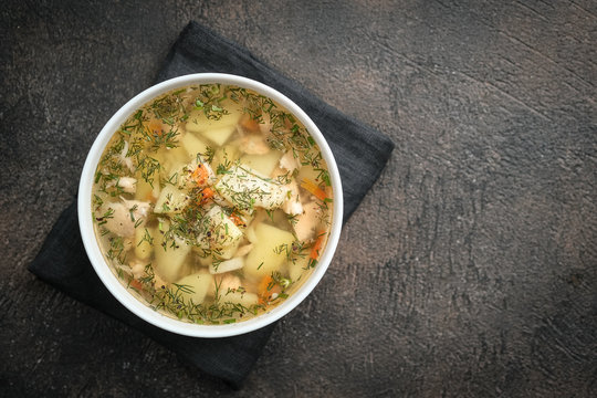 Fresh homemade fish soup with vegetables in bowl on black background, top view with copy space.