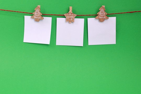 A garland of white empty leaves hanging on a rope on wooden clothespins with Christmas theme on a green background. Christmas decoration. Copy space. Blank paper cards hanging on clothespins. 