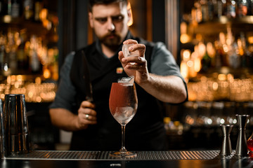 Bartender puts ice cubes in a cocktail drink