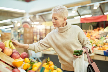 Waist up portrait of beautiful adult woman choosing fresh fruits at farmers market, copy space