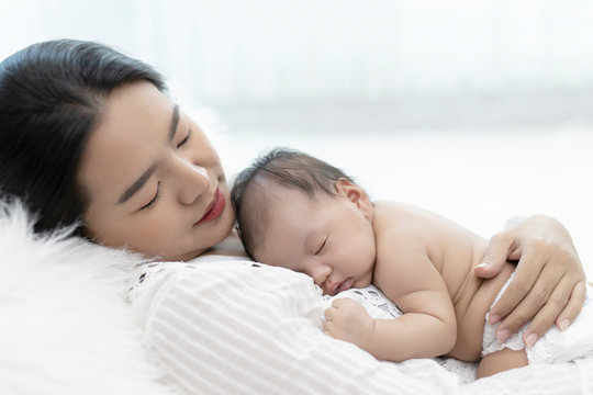 Young mother holding sleeping infant child on hands. Portrait of Asian young with her happy child on arms on white background.