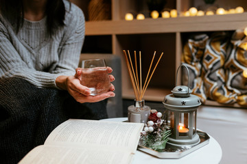 Female in grey knitted sweater holding glass of water wile reading a book - Romantic cozy...