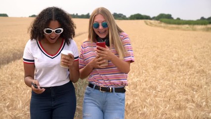 Slow motion tracking video clip of pretty blonde girl and mixed race teenager young women wearing sunglasses drinking coffee and using mobile cell smart phones for social media - Powered by Adobe