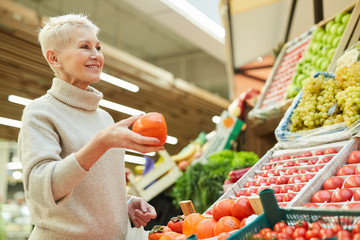 Waist up portrait of smiling adult woman choosing fresh vegetables while grocery shopping at farmers market, copy space