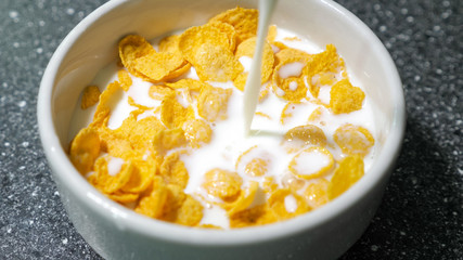 Preparing fast breakfast with cereal. Pouring milk in bowl with dry cornflakes. Traditional morning food.