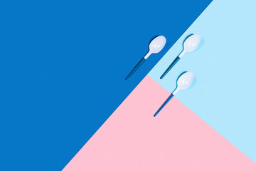 Dangerous and needed three plastic spoons. Environmental problem of plastic rubbish pollution. Three-color background: classic blue, pink and blue. Flat lay, top view, copy space.