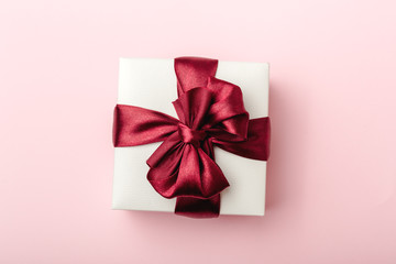 White gift box, with burgundy satin ribbon, pink background, top view