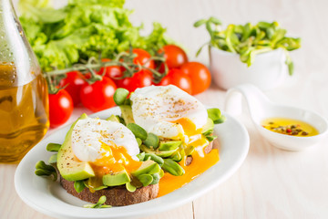 Avocado toast, cherry tomato and poached eggs on wooden background. Breakfast with vegetarian food, healthy diet concept.