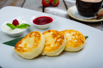 Traditional breakfast with coffee and cheesecakes, cottage cheese pancakes on a plate with syrup and jam.