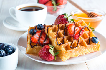 Fresh homemade food of berry Belgian waffles with honey, chocolate, strawberry, blueberry, maple syrup and cream. Healthy dessert breakfast concept with juice