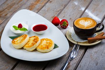 Traditional breakfast with coffee and cheesecakes, cottage cheese pancakes on a plate with syrup and jam.