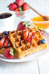 Fresh homemade food of berry Belgian waffles with honey, chocolate, strawberry, blueberry, maple syrup and cream. Healthy dessert breakfast concept with juice