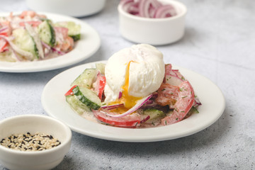 Poached egg on chopped and mixed vegetables with sour cream, white dishes