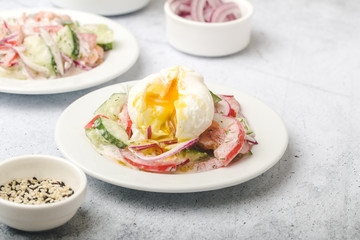 Poached egg on chopped and mixed vegetables with sour cream, white dishes, gray, stone background