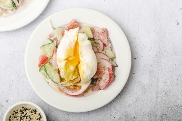 Poached egg on chopped and mixed vegetables with sour cream, scattered sesame seeds, white dishes