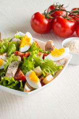 Fresh Caesar salad with delicious chicken breast, ruccola, spinach, cabbage, arugula, egg, parmesan and cherry tomato on wooden background. Oil, salt and pepper. Healthy and diet food concept.