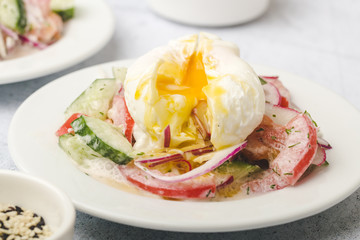 Poached egg on chopped and mixed vegetables with sour cream, white dishes, gray background