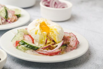 Poached egg on chopped and mixed vegetables with sour cream, white dishes