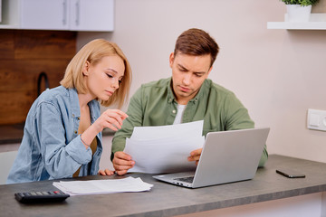 beautiful lovely young couple reading and analyzing bills sitting at table and using modern laptop. Young couple in casual discussing home economics