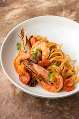 Mediterranean cuisine, pasta with king prawns, brown stone background.