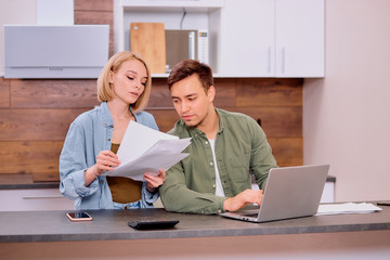 couple checking analyzing utilities bills sitting together at kitchen table, husband and beautiful...