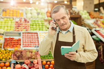Waist up portrait of senior man speaking by smartphone while ordering fresh fruits and vegetables at farmers market, copy space
