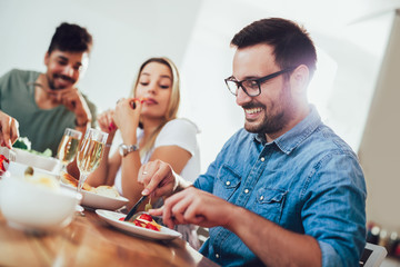Cheerful young people enjoying meal while sitting at the dinning table on the kitchen together.