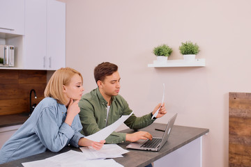handsome caucasian man explain and talk with woman at home using laptop, holding documents, wearing...