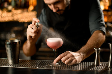 Fototapeta na wymiar Bartender spraying small glass with alcohol cocktail