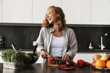 Happy young woman making a salad at the kitchen