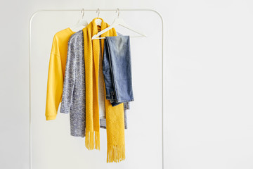 Female clothes in yellow and blue color on hanger on white background.  Jumper, shirt and scarf. Spring/autumn outfit. Minimal concept.