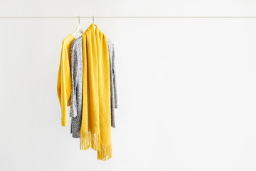 Female clothes in yellow and blue color on hanger on white background.  Jumper, shirt and scarf....