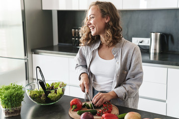 Happy young woman making a salad at the kitchen